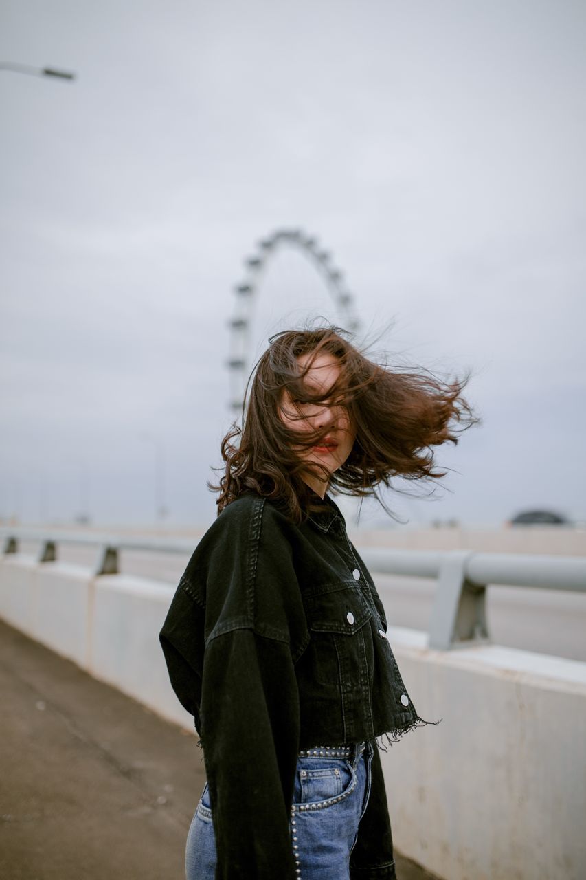 one person, standing, focus on foreground, sky, real people, lifestyles, waist up, leisure activity, casual clothing, hairstyle, nature, women, young adult, hair, young women, clothing, adult, three quarter length, outdoors, warm clothing, wind, beautiful woman