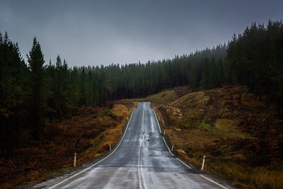 Road amidst trees in forest against sky