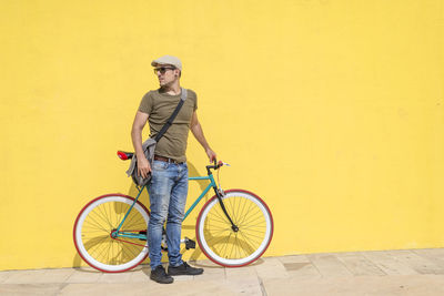 Mid adult man with bicycle standing against yellow wall