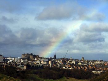 Buildings against rainbow in cloudy sky