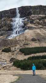 Full length of man on road against waterfall and mountain