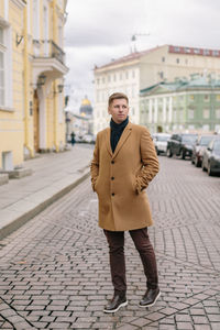 Attractive man in beige coat, with blue scarf tied around his neck, brown pants and leather shoes