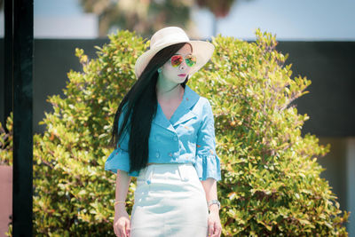 Young woman wearing hat standing against plants