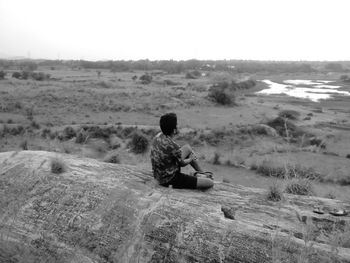 Rear view of man sitting on mountain against landscape