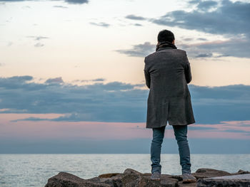 Rear view of man standing by sea against sky