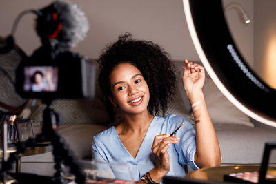 Smiling young woman applying shades with brush on hand while recording on camera at home