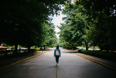 Rear view of woman walking on road amidst trees in city