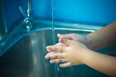 Close-up of child washing hand under faucet