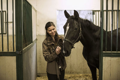 Smiling young woman with horse in stable