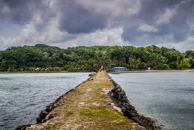 Pathway amidst river against cloudy sky at dusk