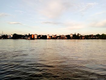 Sea by buildings against sky during sunset