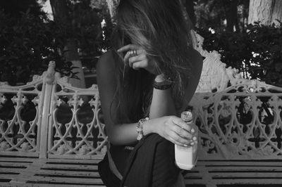 Woman having drink while sitting on bench