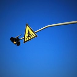 Low angle view of road sign against clear blue sky