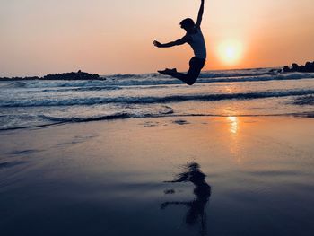 Man jumping on beach against sky during sunset