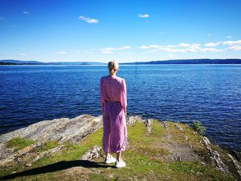 Rear view of woman standing on rock formation against sky