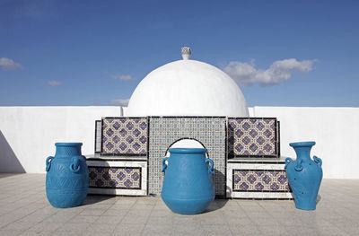 Blue urns by traditional built structure against sky