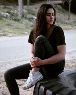 Thoughtful young woman sitting on tire at roadside