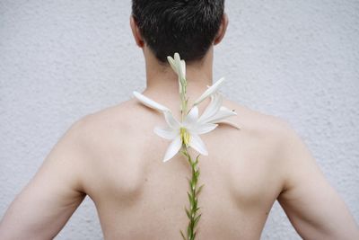 Rear view of shirtless man with flowers against white wall