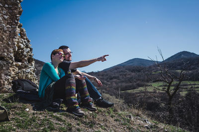 Couple sitting on mountain against clear blue sky