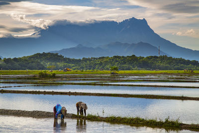 People on lake by mountains against sky