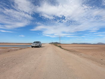 Car on road amidst desert against sky