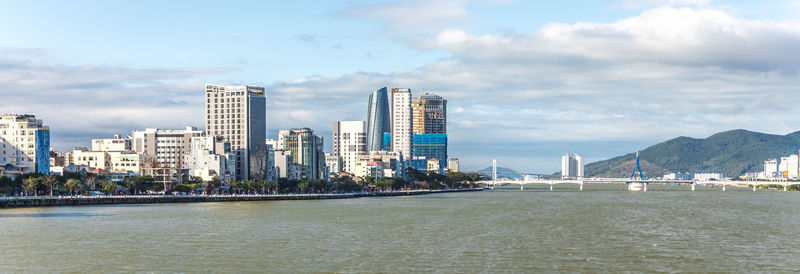 City by river and buildings against sky