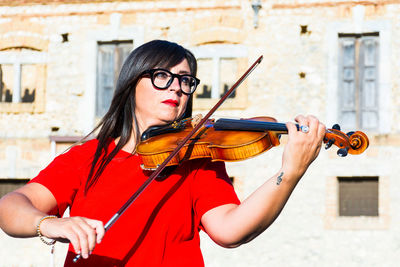 Woman playing violin while standing against building in city