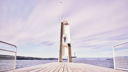 Woman standing on diving platform by river against sky