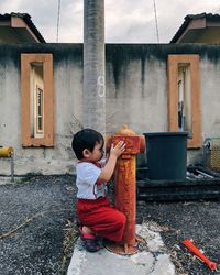 Full length of boy holding fire hydrant against building