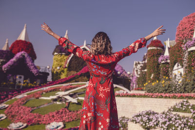 Rear view of young woman standing in ornamental garden against sky 