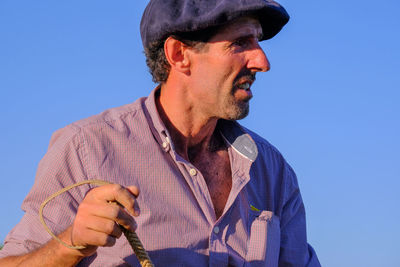 Low angle view of man looking away against clear blue sky