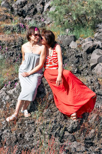 Two young hippie women sitting embraced on the lava rock on hillside of etna.