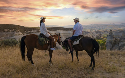 Rear view of man riding horse on field against sky during sunset