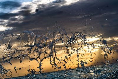 Water splashing in sea against sky during sunset