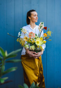 Young woman in flowing yellow skirt and white shirt with beautiful bouquet of peonies in glass vase