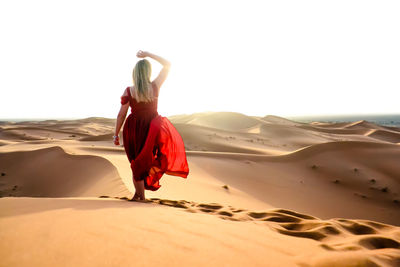 Rear view of woman walking on sand at beach against clear sky