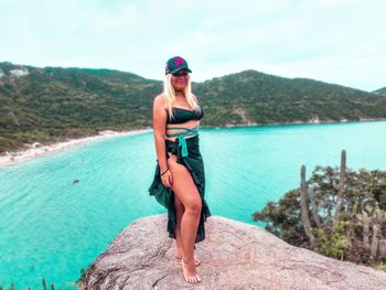 Full length of woman on rock at sea shore against sky