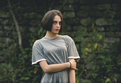 Young woman looking away while standing against wall