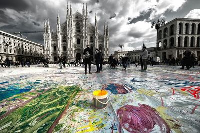 People walking on city street against cloudy sky