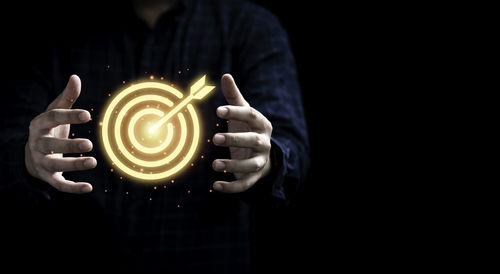 Midsection of man holding illuminated light against black background