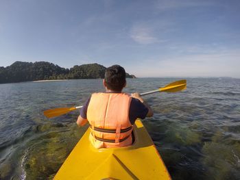 Rear view of man in kayak on sea against sky