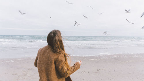 Rear view of woman on beach against sky