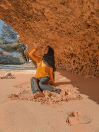 Full length of young woman sitting by rock outdoors