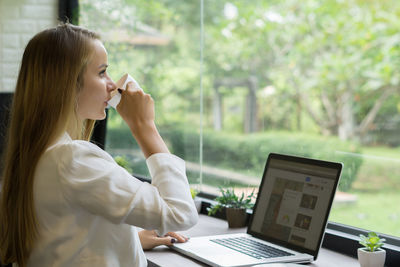 Businesswoman drinking coffee while using laptop in office