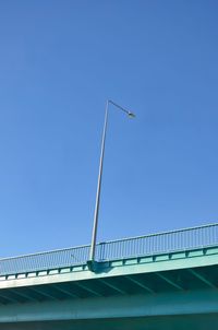 Low angle view of bridge with streetlight against clear blue sky