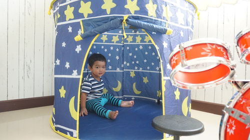 Full length portrait of cute boy sitting in tent at home