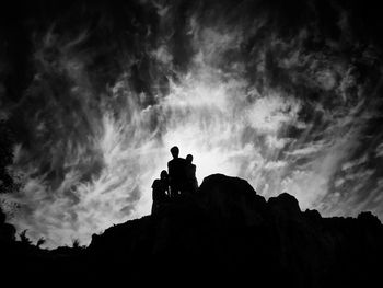 Low angle view of silhouette people on rock formation against cloudy sky