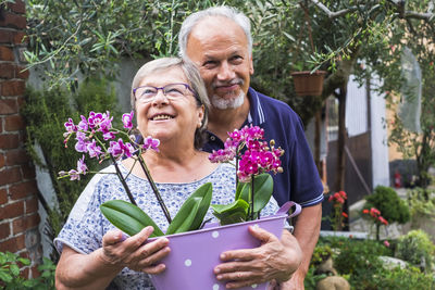 Smiling couple with potted plants standing at yard