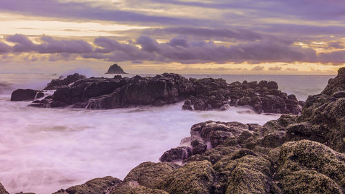 Rocks on beach against sky during sunset