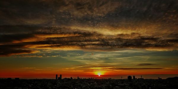 Silhouette cityscape against dramatic sky during sunset